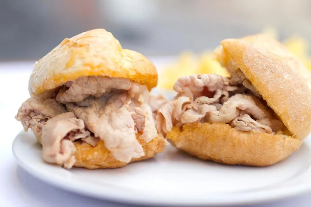 Duas bifanas em pão num prato, batatas fritas atrás